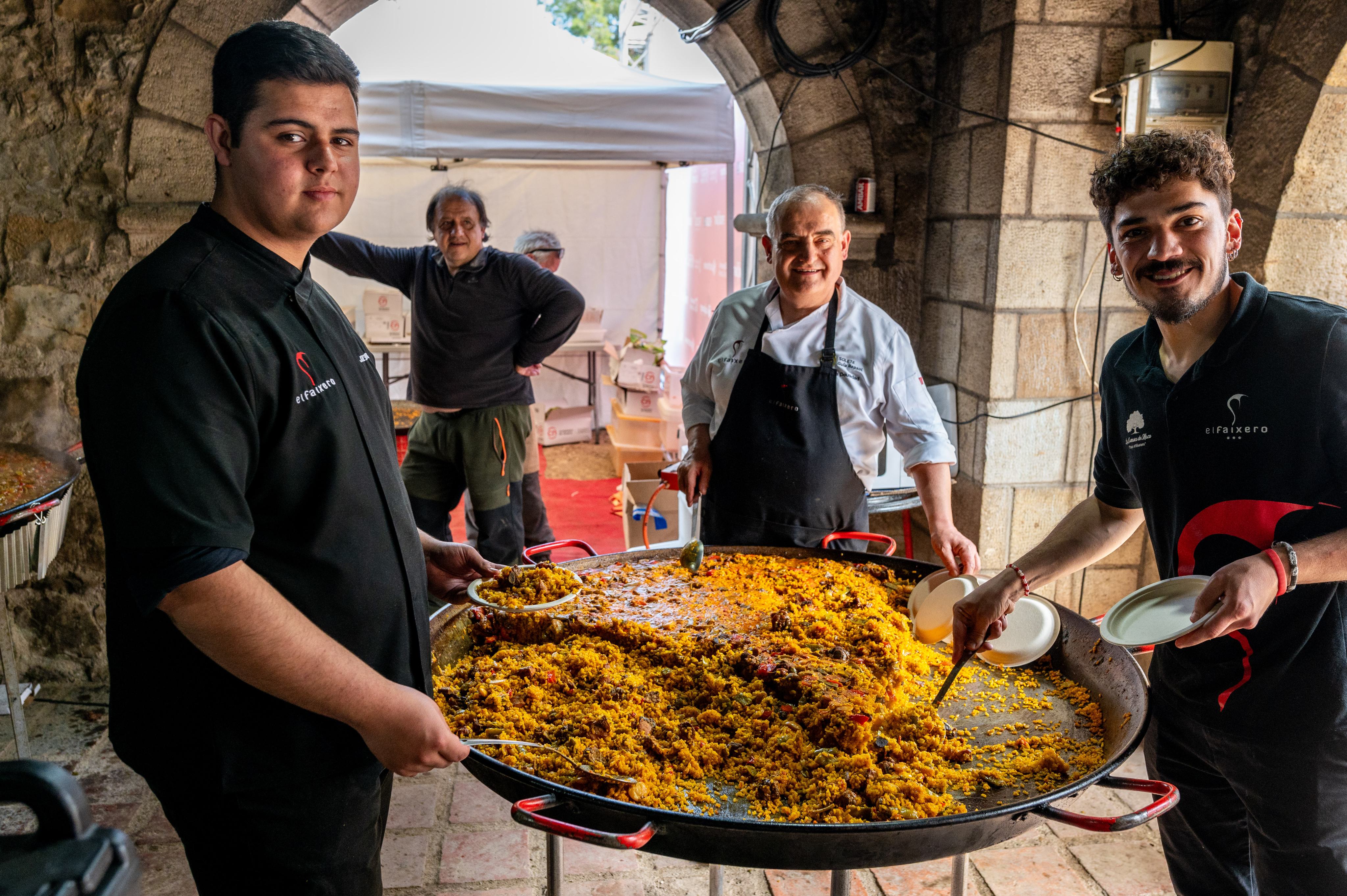 Personas mostrando una paella grande junto a un edificio de piedra
